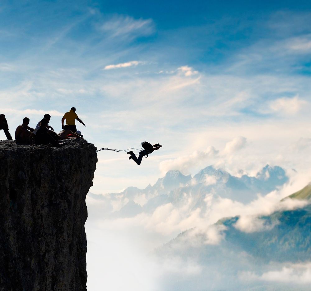 Person jumping off a cliff with team support.